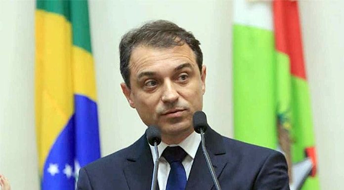 carlos moisés falando em dois microfones com bandeiras de brasil e sc ao fundo