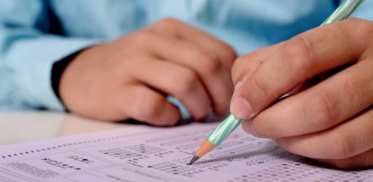 18 concursos públicos: close em mãos de homem segurando lápis fazendo anotações em tabela de resposta