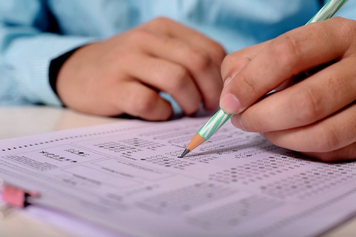 18 concursos públicos: close em mãos de homem segurando lápis fazendo anotações em tabela de resposta