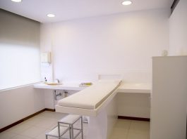 consultório com cama no meio, tudo organizado; pia e armários ao lado