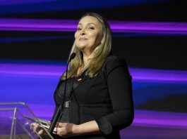 Daniela Cristina Reinehr Koelzer, primeira mulher governadora de Santa Catarina daniela vista sorridente e altiva em frente à tribuna transparente com microfone