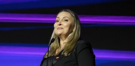 daniela vista sorridente e altiva em frente à tribuna transparente com microfone