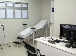 consultório do posto de saúde; com maca ao fundo e mesa com cadeira e computador em primeiro plano