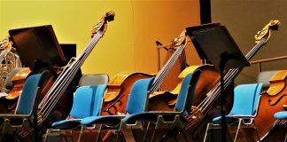 instrumentos musicais como violoncelos e contrabaixos apoiados ao lado de cadeiras de orquestra