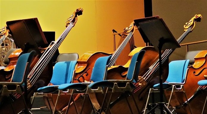 instrumentos musicais como violoncelos e contrabaixos apoiados ao lado de cadeiras de orquestra
