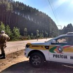 policia rodoviário em frente à caminhonte da PMRV na beira de estrada; plantação de eucalipto ao fundo