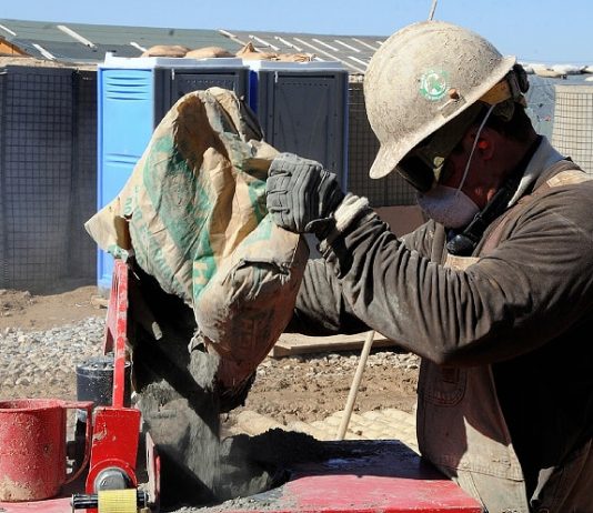Pedreiros são os profissionais autônomos mais solicitados durante a pandemia em Santa Catarina trabalhador da construção civil usando máscara, capacete e óculos de proteção faz preparo de cimento em cima de bancada em área de construção