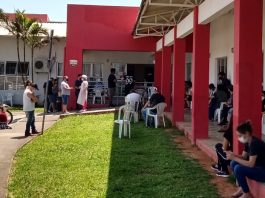gramado com cadeiras em frente ao cati onde há pessoas em volta usando máscaras esperando em filas e sentadas em volta