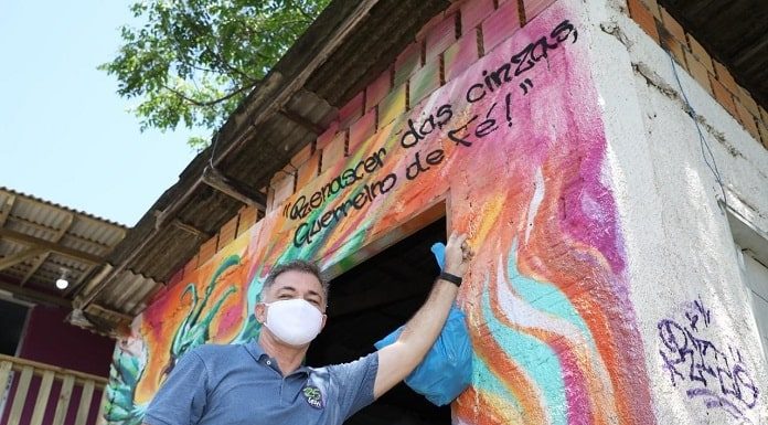 foto de baixo para cima de gean usando máscara e apoiado em parede pintada com dizeres escritos