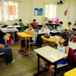 Crianças sentadas em carteiras de sala de aula olhando para professora