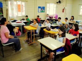 Crianças sentadas em carteiras de sala de aula olhando para professora