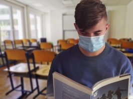 Governo de Reinehr autoriza volta às aulas presenciais na faixa laranja em Santa Catarina aluno usando máscara lê um livro de frente para a foto; cadeiras de sala de aula ao fundo