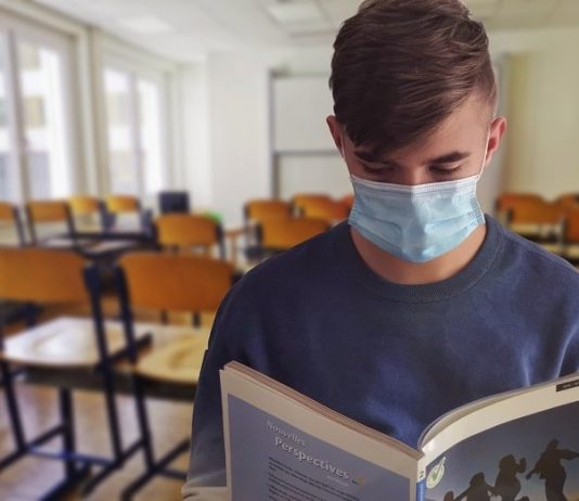 Fecam considera que retorno das aulas não significa recuperação de conteúdo neste ano aluno usando máscara lê um livro de frente para a foto; cadeiras de sala de aula ao fundo