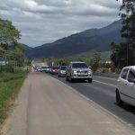 carros passando em fila na estrada e acostamento no centro da imagem