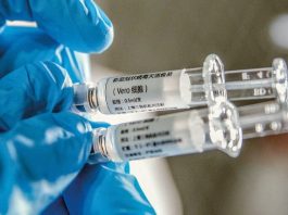 pessoas usando luva azul cirúrgica segura duas seringas de vacina com dizeres em chinês