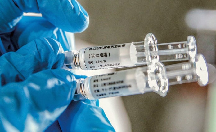pessoas usando luva azul cirúrgica segura duas seringas de vacina com dizeres em chinês