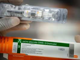 close em mãos de pessoa segurando caixa da vacina de covid-19 e uma dose fora da caixa