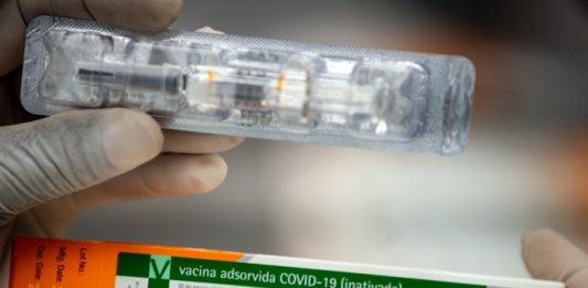 close em mãos de pessoa segurando caixa da vacina de covid-19 e uma dose fora da caixa