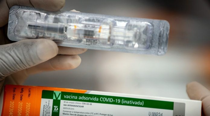 close em mãos de pessoa segurando caixa da vacina de covid-19 e uma dose fora da caixa