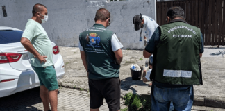 três homens de costas, fiscalizando um esgoto e outro homem mexendo com um material no esgoto