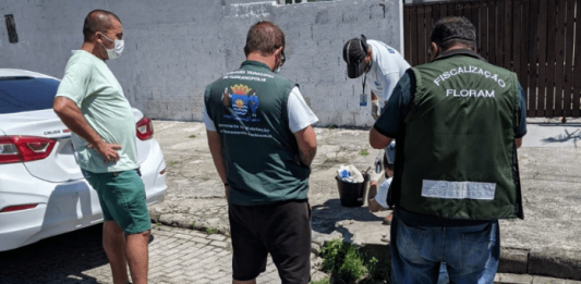três homens de costas, fiscalizando um esgoto e outro homem mexendo com um material no esgoto