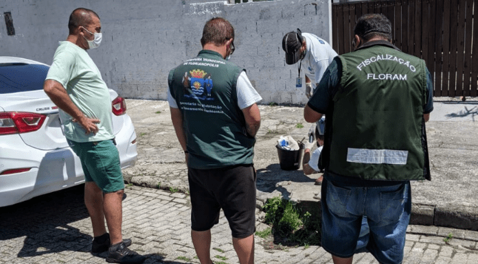 três homens de costas, fiscalizando um esgoto e outro homem mexendo com um material no esgoto