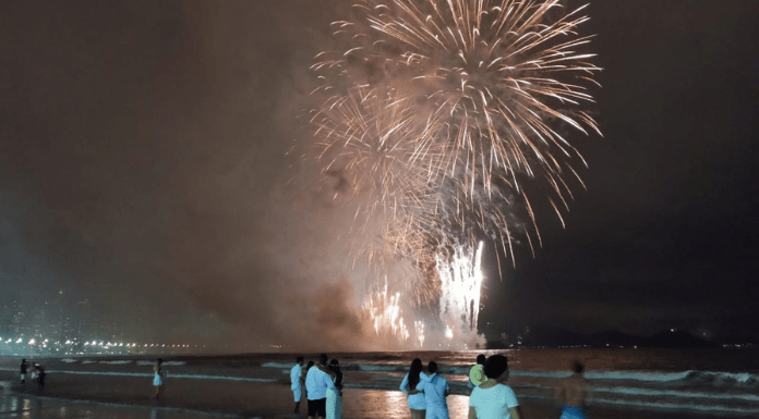 Queima de fogos na praia com pessoas olhando