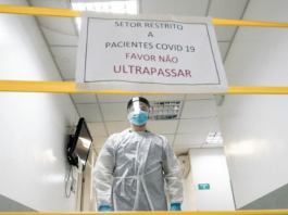 Área restrita em hospital, com cartaz, fitas amarelas e médico equipado contra o coronavírus