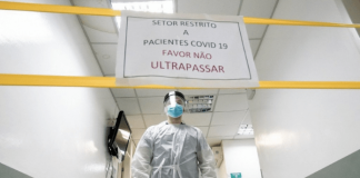 Área restrita em hospital, com cartaz, fitas amarelas e médico equipado contra o coronavírus