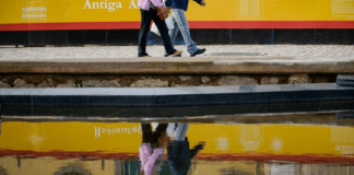 Duas pessoas caminhando na calçada e o reflexo delas na água