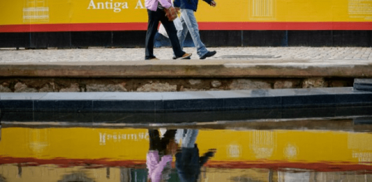 IBGE aponta que expectativa de vida de Santa Catarina é a maior do País Duas pessoas caminhando na calçada e o reflexo delas na água