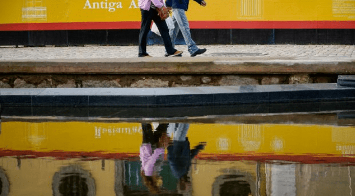 Duas pessoas caminhando na calçada e o reflexo delas na água