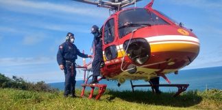 dois tripulantes ao lado do helicoptero pousado em área de gramado