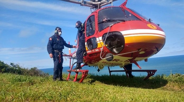 dois tripulantes ao lado do helicoptero pousado em área de gramado