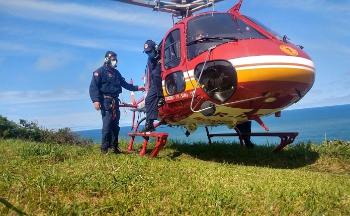 dois tripulantes ao lado do helicoptero pousado em área de gramado