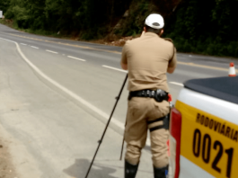Feriado de Finados nas estradas de SC tem 8 mortes em acidentes Rodovia catarinense, com policial em pé, de costas para a foto e no canto direito o carro da Polícia Militar
