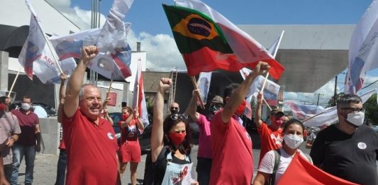 ary martins levanta a mão cerrada em comemoração com diversos correligionários em volta com bandeiras