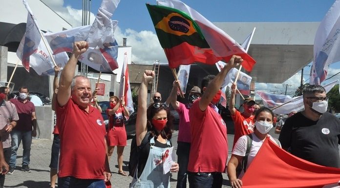 ary martins levanta a mão cerrada em comemoração com diversos correligionários em volta com bandeiras