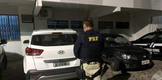 Policial com uniforme da PRF de costas em frente ao veículo