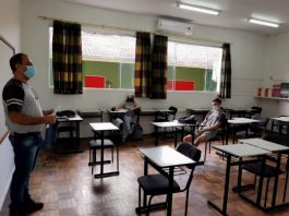 professor usando máscara dá aula para dois alunos, maioria das carteiras vazias