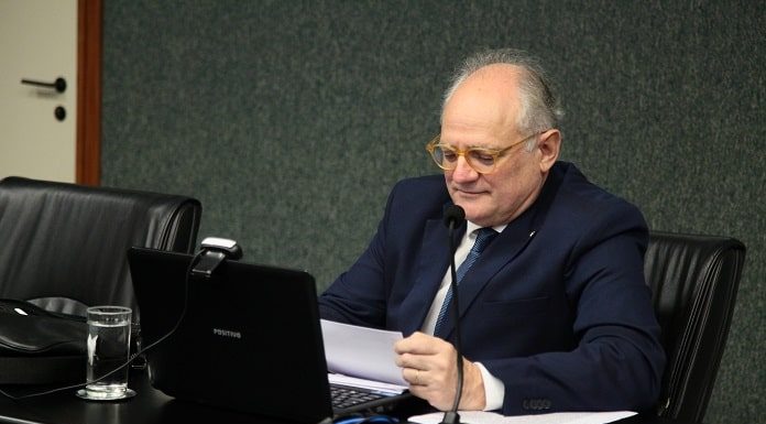 deputado vicente caropreso sentando atrás de mesa com notebook olha pra um documento
