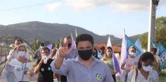 fernando anselmo usa máscara e faz sinal com a mão para cima e atrás correligionários em caminhada usando máscaras e com bandeiras