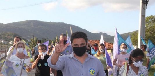 fernando anselmo usa máscara e faz sinal com a mão para cima e atrás correligionários em caminhada usando máscaras e com bandeiras