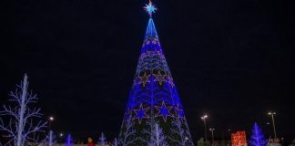 estrutura de ávore de natal iluminada com estrelas e outros elementos de decoração em volta