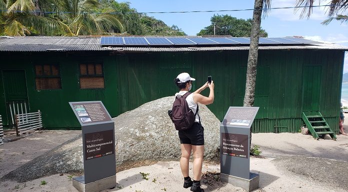 Mulher tira fotos no sítio arqueológico da ilha do Campeche, ela está próxima às placas instaladas com informações do local.