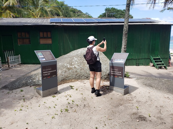 Mulher tira fotos no sítio arqueológico da ilha do Campeche, ela está próxima às placas instaladas com informações do local.