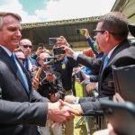 bolsonaro sorridente aperta mão de agente da prf com pesosas em volta filmando com celulares; algumas sem máscara; presidente sem máscara