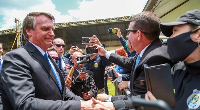 bolsonaro sorridente aperta mão de agente da prf com pesosas em volta filmando com celulares; algumas sem máscara; presidente sem máscara