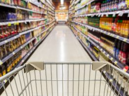 carrinho de supermercado posicionado em um corredor entre prateleiras de produtos