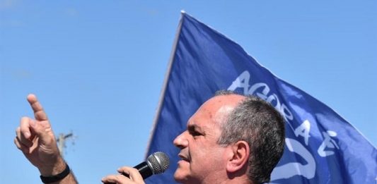 A chance de mudar é agora moacir visto de lado discursando ao microfone com dedo em riste; bandeira com seu número ao fundo